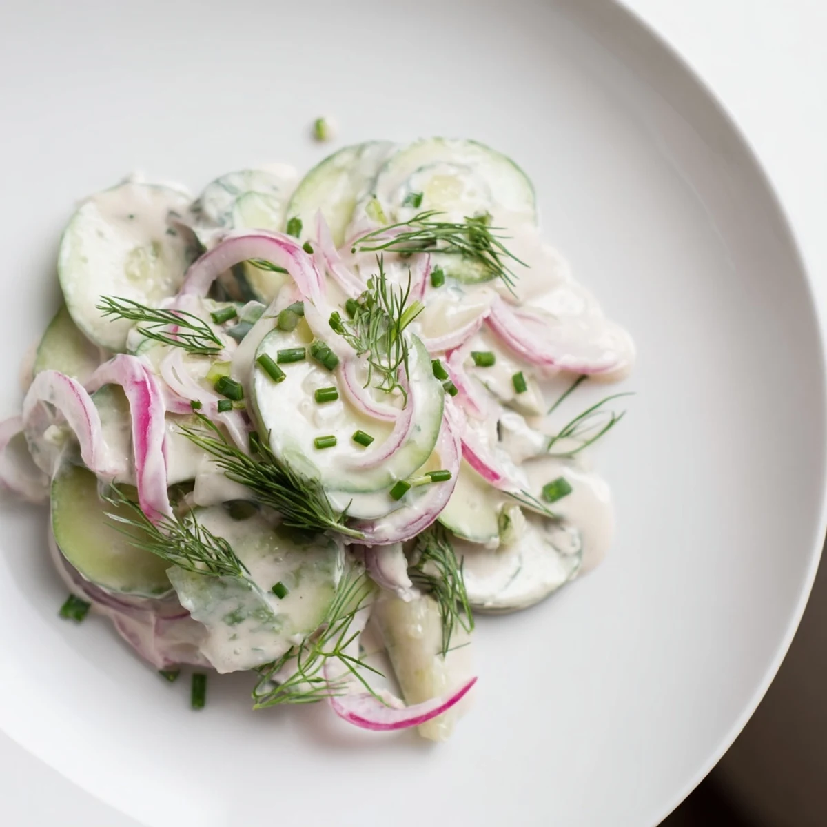 Creamy German Cucumber Salad in a white bowl, showing fresh sliced cucumbers and herbs with a bright, cool dressing.