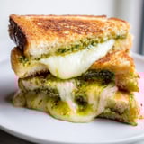 Ein geröstetes Sourdough Pesto Grilled Cheese Sandwich mit schmelzendem Käse und frischem Basilikum.