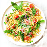 Frühlingsspargel und Erbsen in einer Frühlings-Gemüse-Einpott-Spaghetti mit Parmesan und Basilikum garniert, auf weißem Hintergrund serviert.