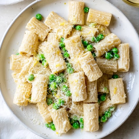 Rigatoni mit Erbsen und Zitronen-Ricotta wird frisch und cremig auf einem Teller angerichtet.
