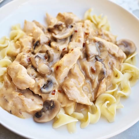 Ein Teller Chicken Stroganoff mit glänzender Soße, frischer Petersilie und cremigen Eiernudeln serviert.